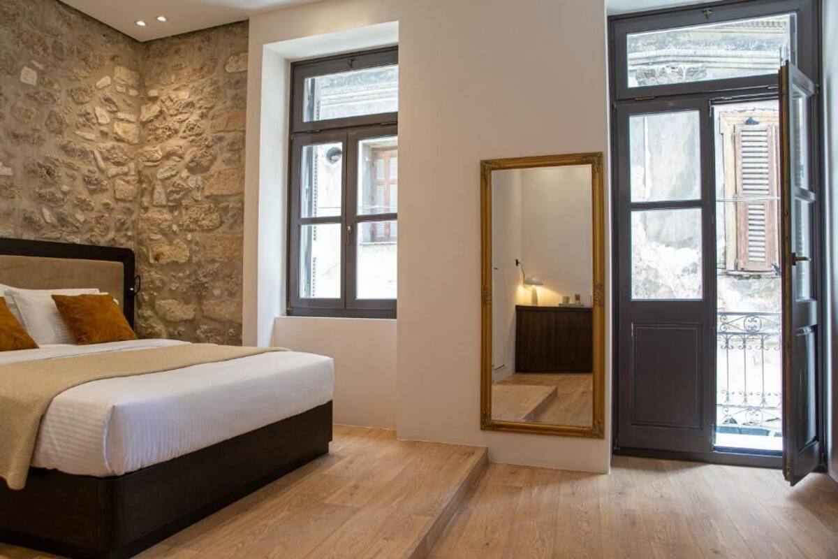 A bedroom with a stone wall, a bed with a headboard, two windows, and a large mirror.