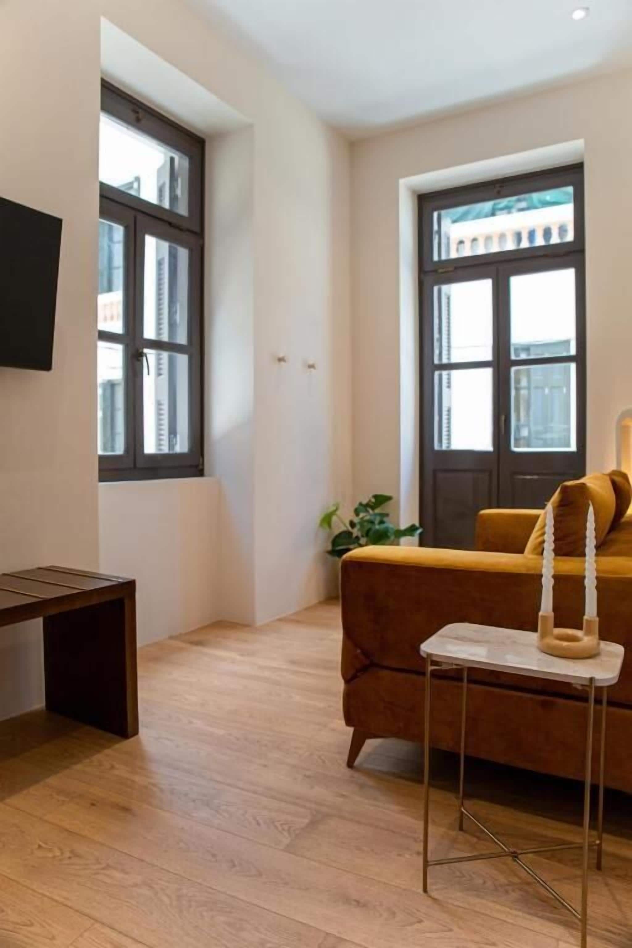 Un salon moderne avec un plancher en bois, un canapé marron, une petite table et un téléviseur fixé au mur.