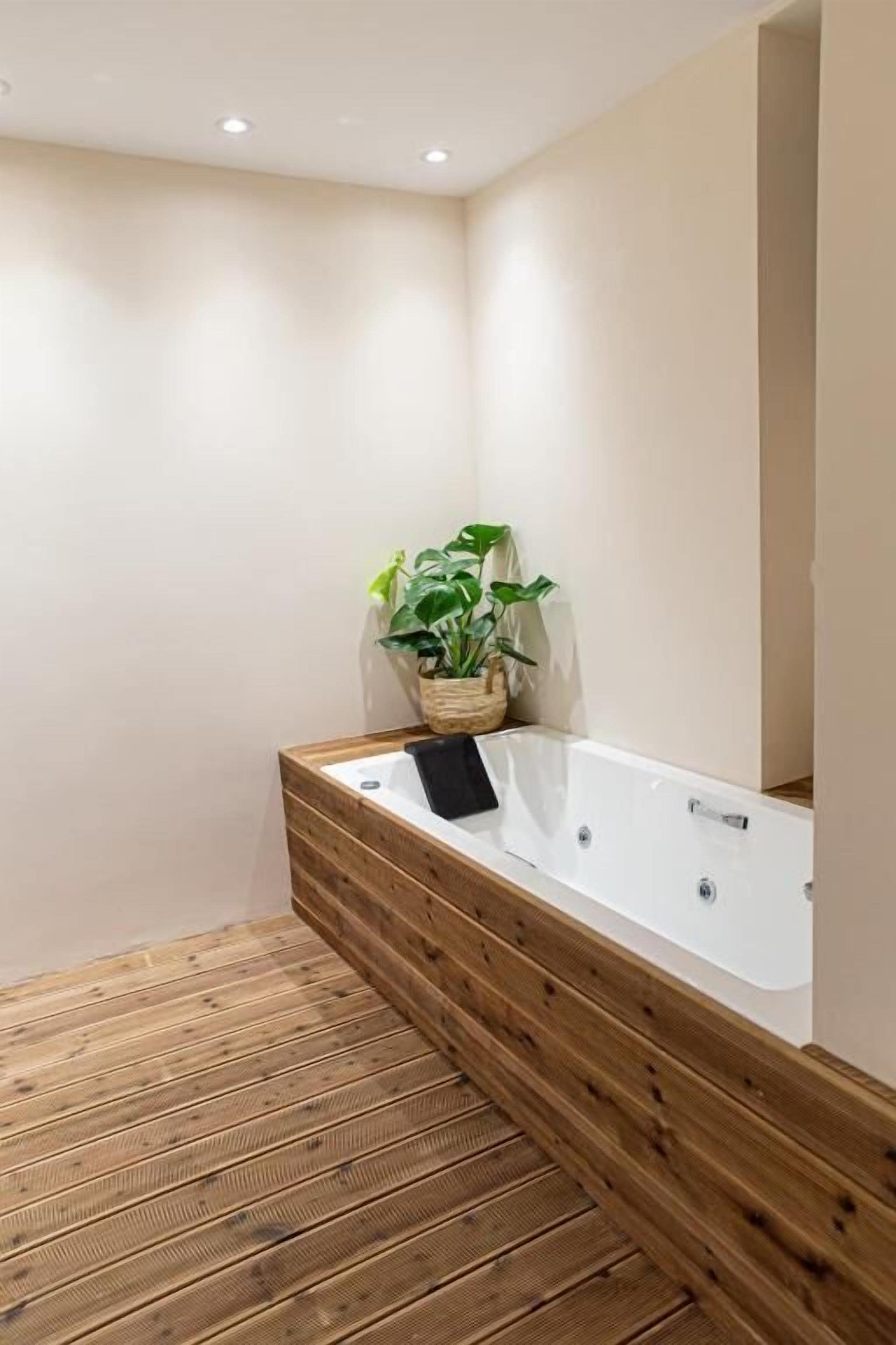 A modern bathroom with a wooden bench, a white bathtub, and a potted plant.