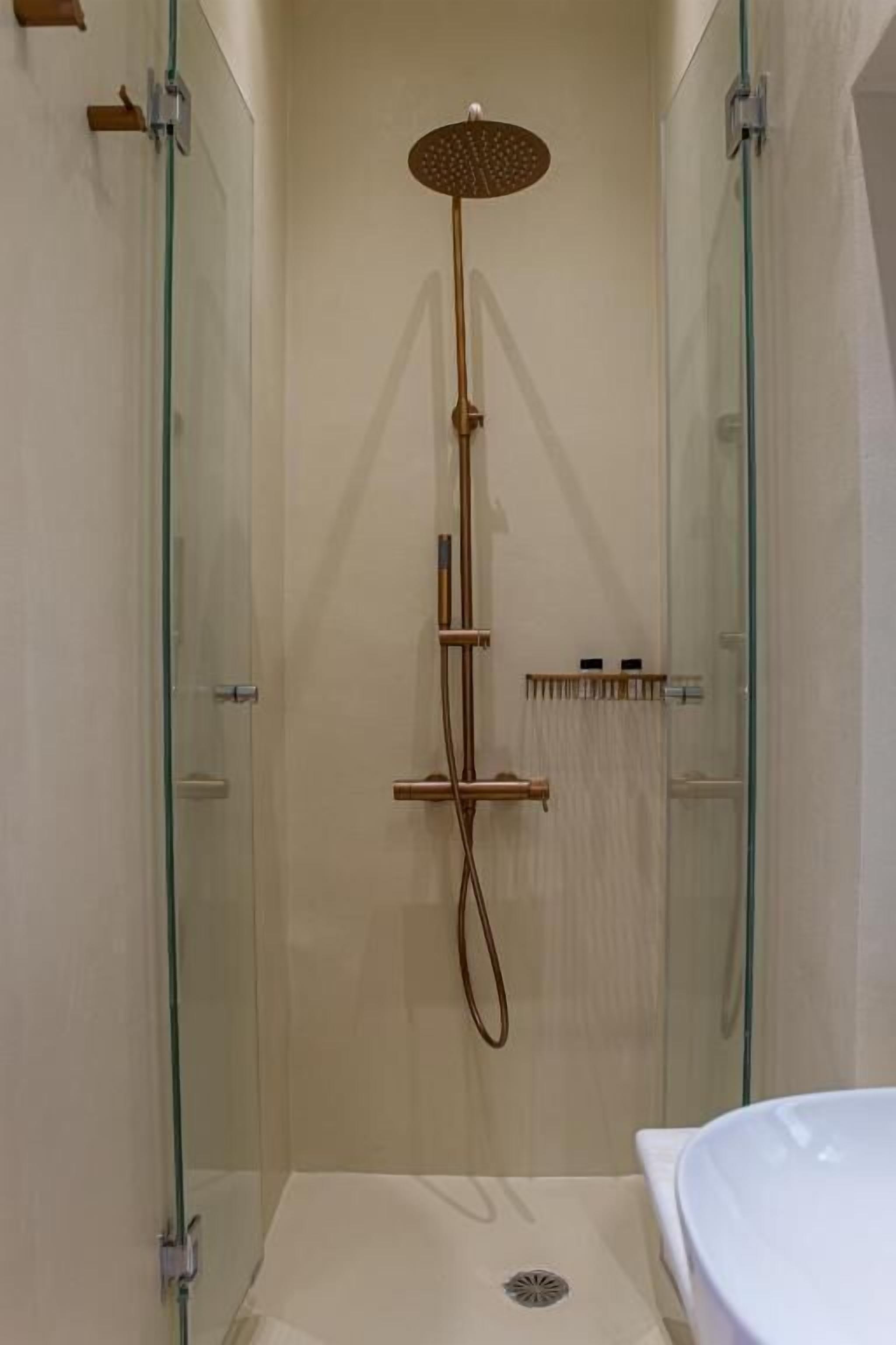 A glass-enclosed shower with a handheld showerhead and a wall-mounted control panel.