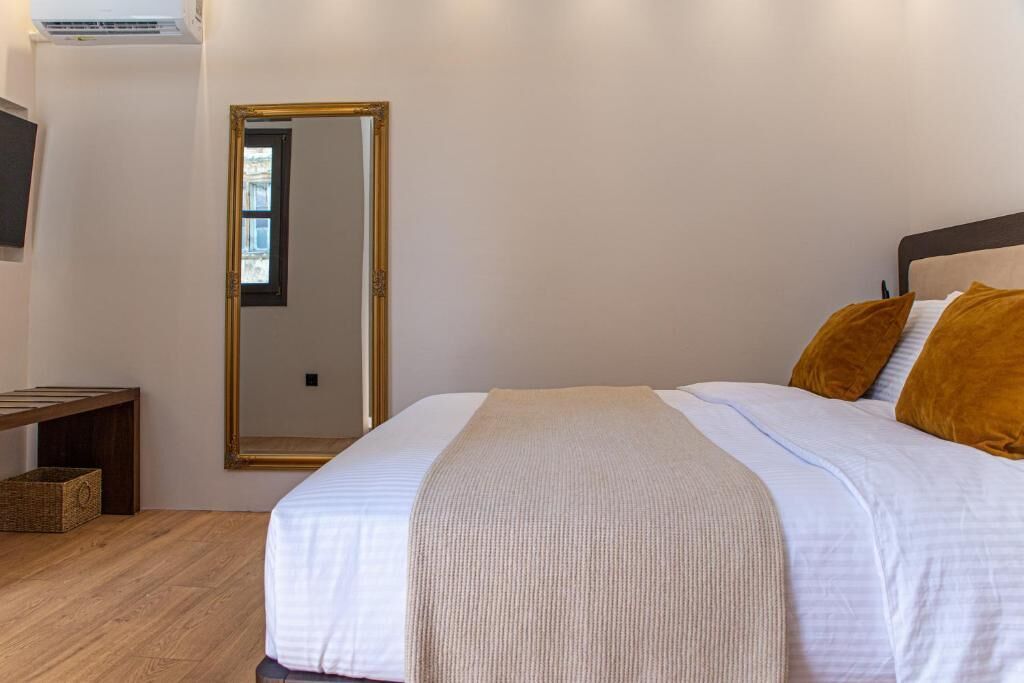 A bedroom with a bed, a mirror, a wooden bench, and a small basket.