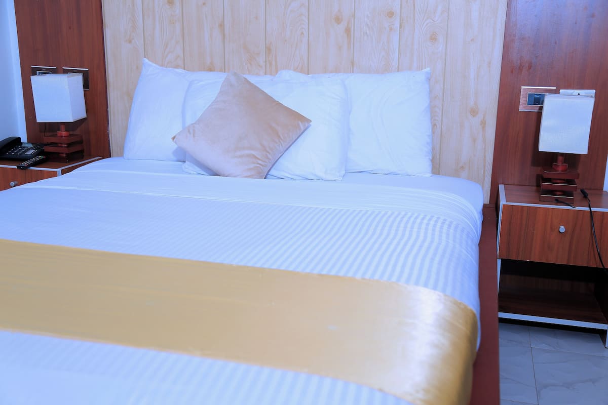 Habitación de hotel con una cama grande, cabecero de madera, mesitas de noche con lámparas y un teléfono.