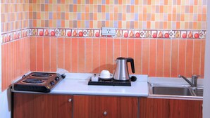 A kitchen with wooden cabinets, a tiled backsplash, and a countertop with a kettle and a coffee pot. - Abat Guest House (Addis Ababa)