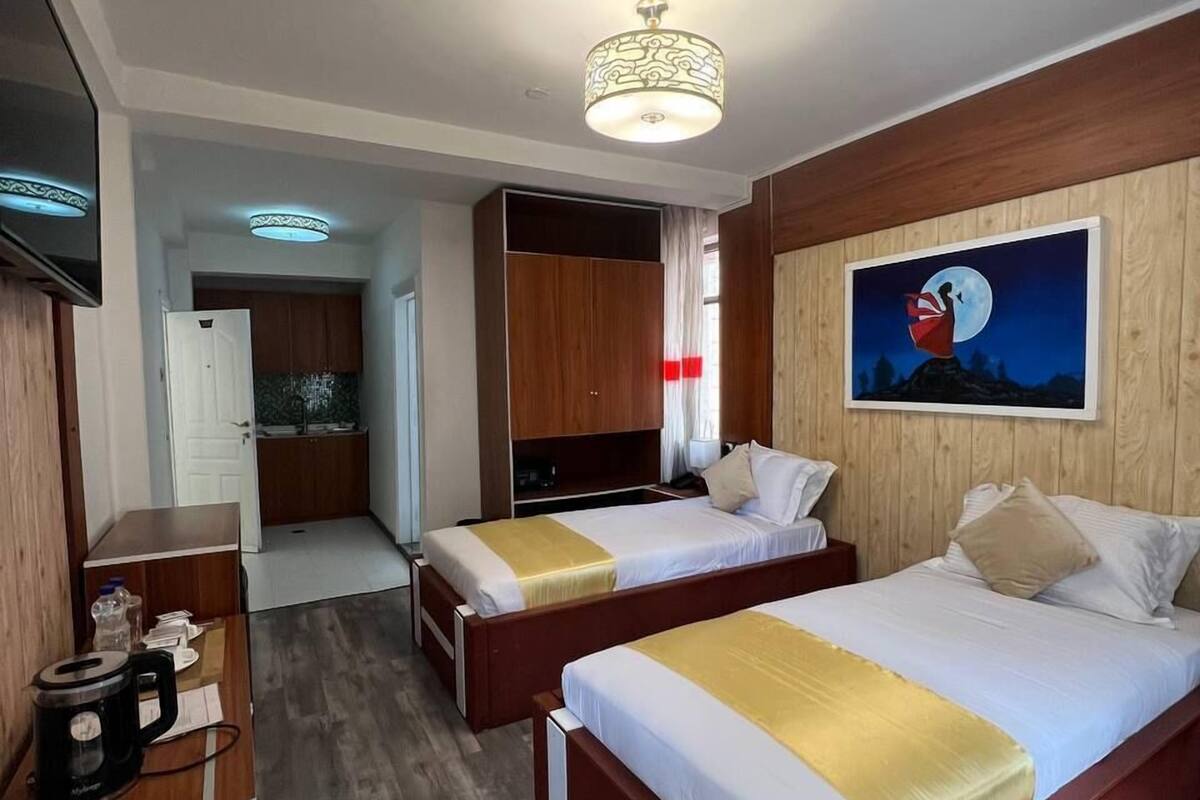Habitación de hotel con dos camas, un escritorio, una cafetera y un cuadro de una escena iluminada por la luna.