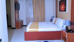 A hotel room with a bed, bedside table, lamp, and a TV mounted on the wall. - Abat Guest House (Addis Ababa)