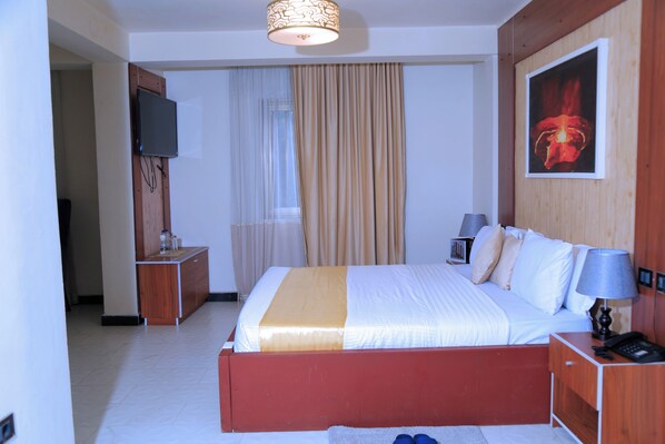 A hotel room with a bed, bedside table, lamp, and a TV mounted on the wall.