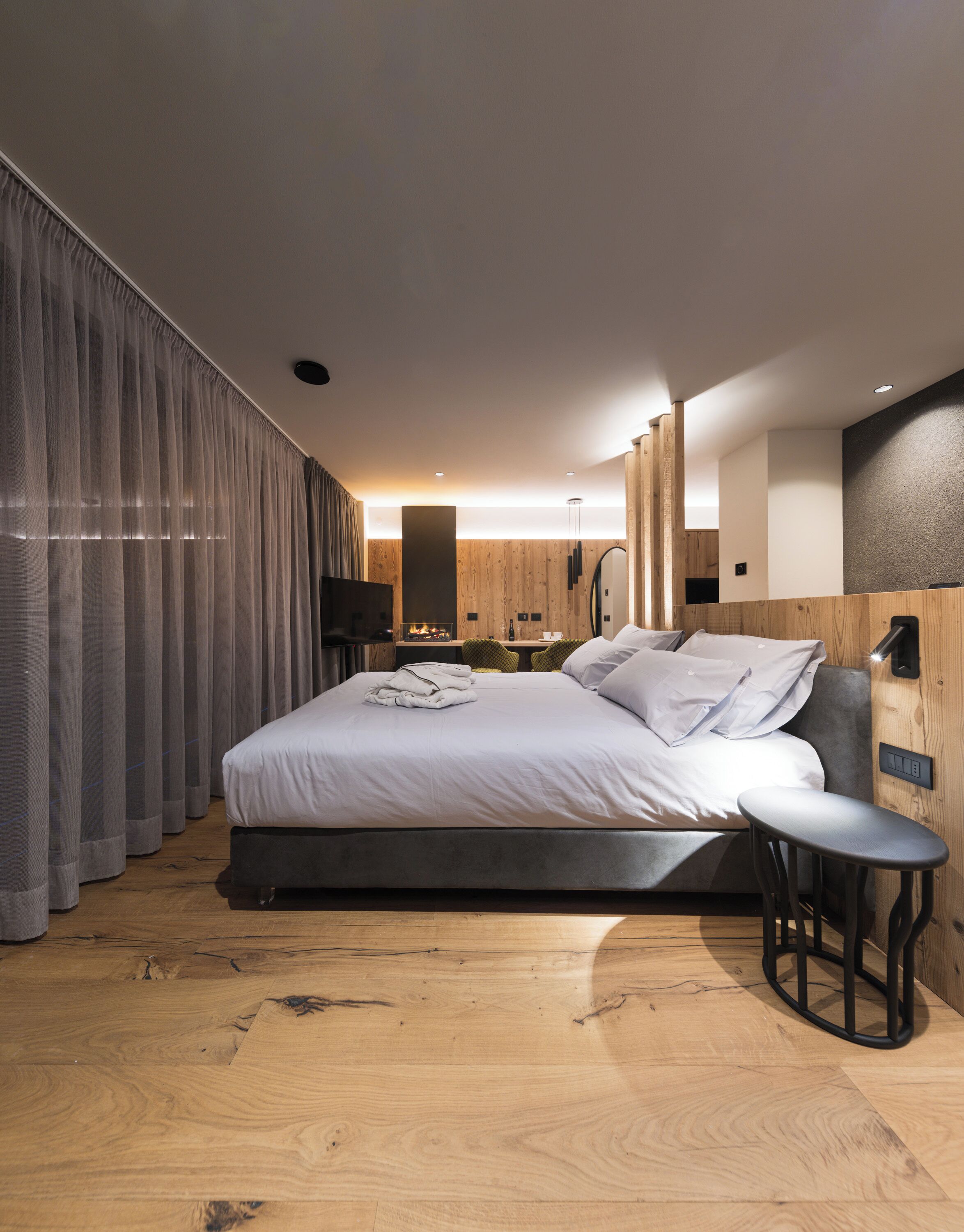 A modern bedroom with a large bed, wooden flooring, and a small table.