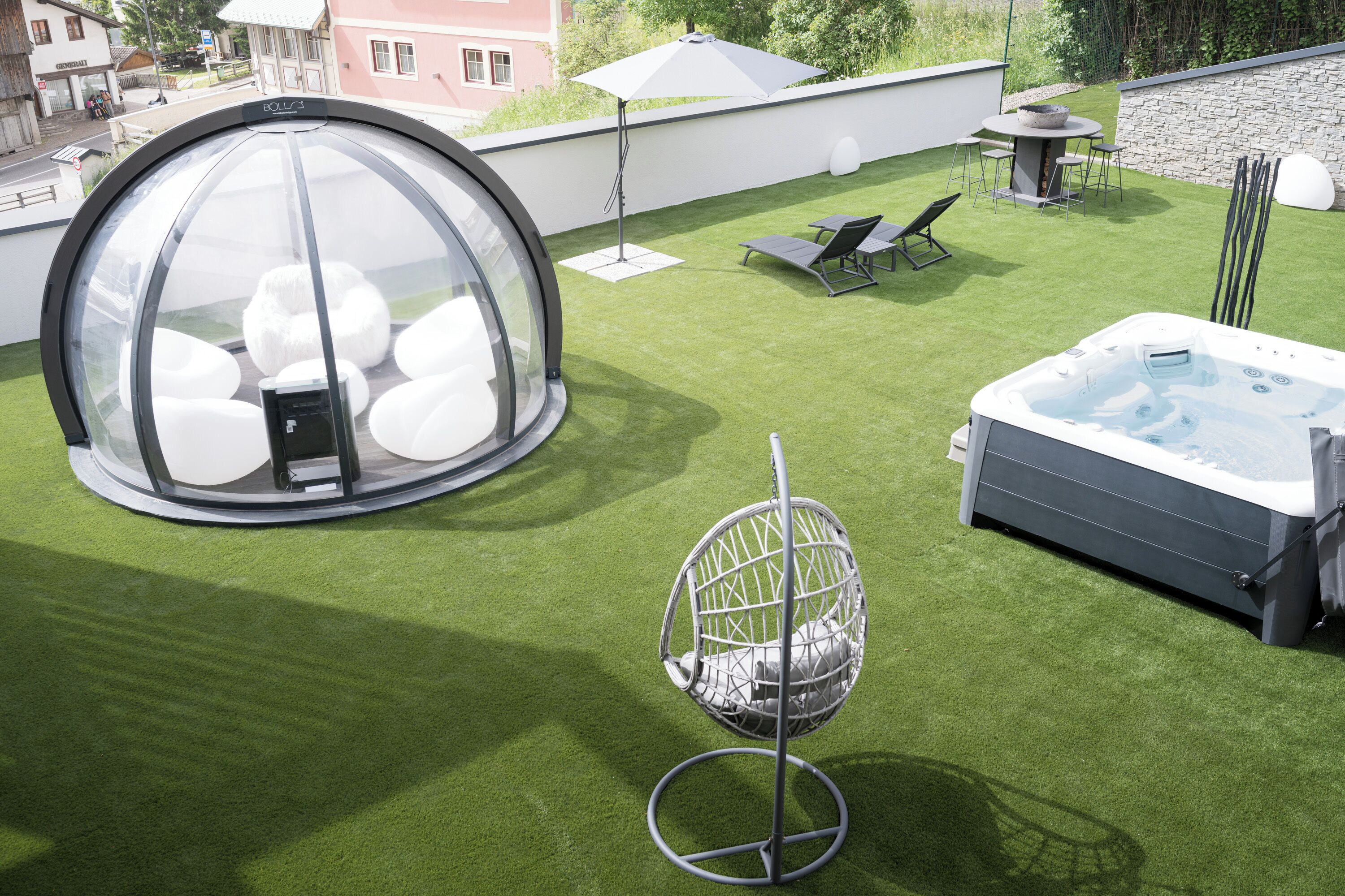 Una terraza con un jacuzzi, una estructura de vidrio esférica y una silla colgante.