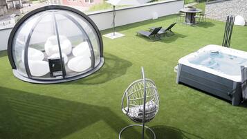 Una terraza con un jacuzzi, una estructura de vidrio esférica y una silla colgante.