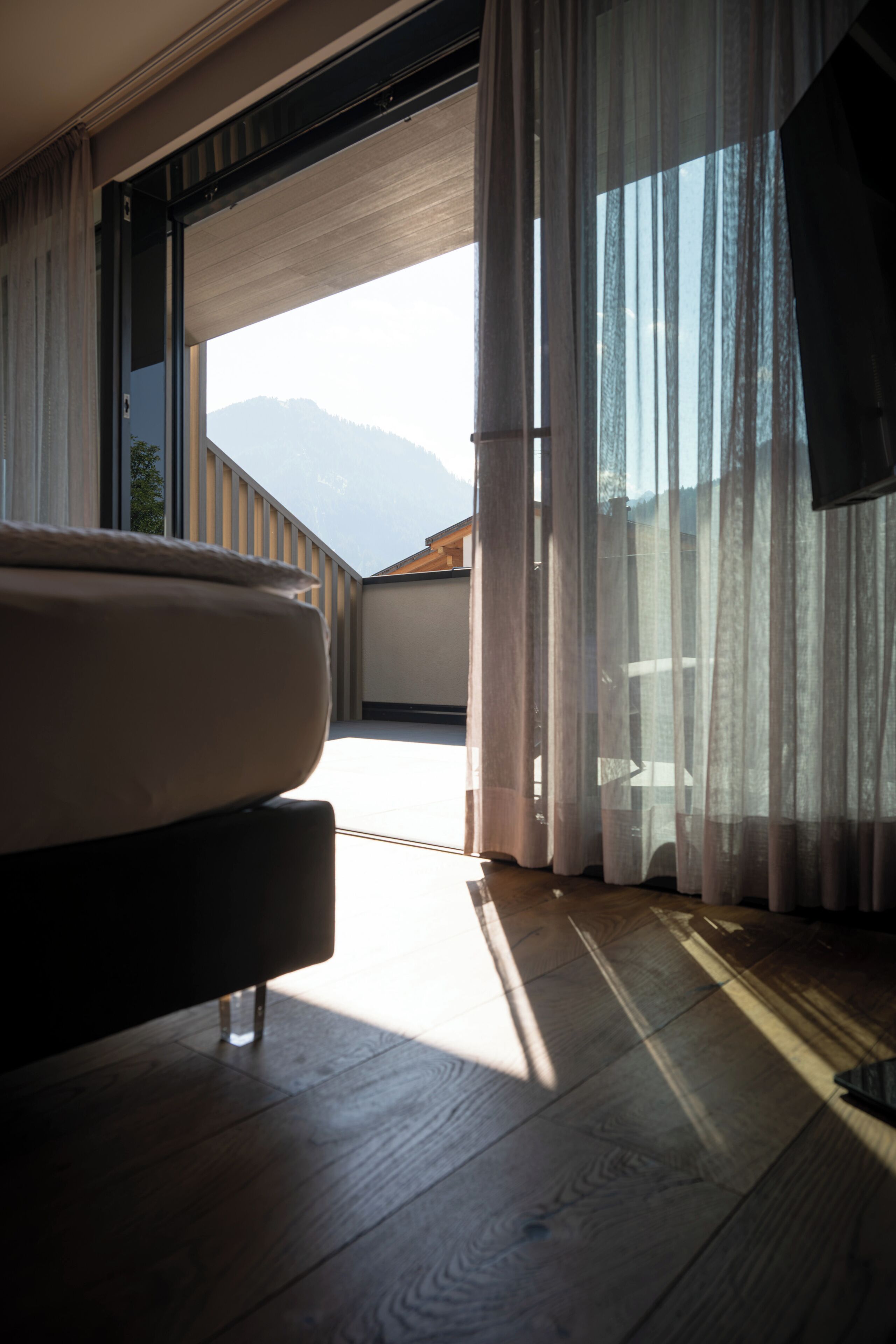 Una habitación con cama, ventana con cortinas translúcidas y vistas a las montañas.