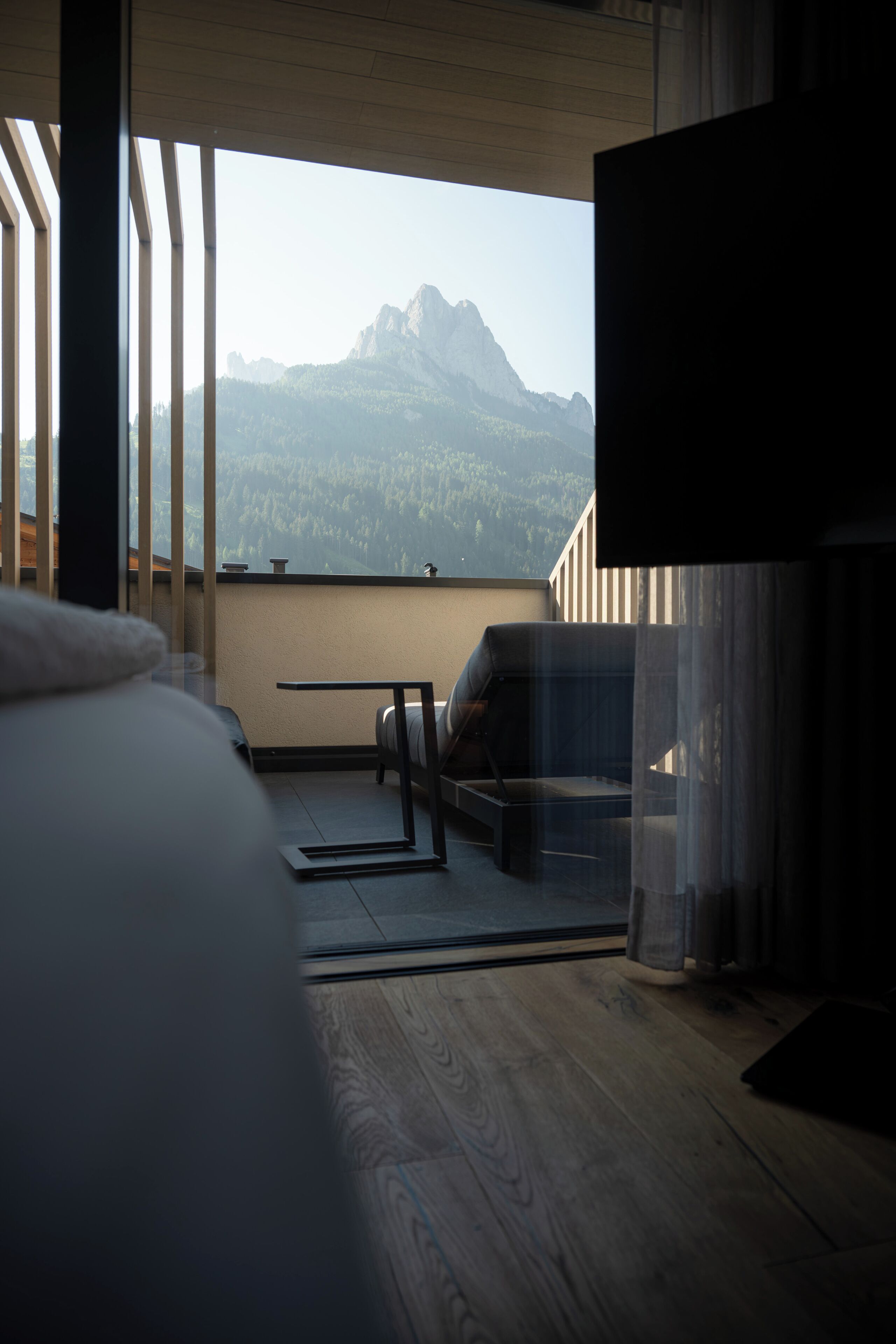 A bedroom with a large bed, a TV, and a balcony with a view of mountains.