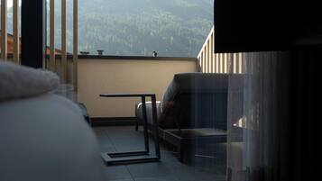 A bedroom with a large bed, a TV, and a balcony with a view of mountains.