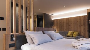 A modern bedroom with a large bed, a round side table, and wooden paneling on the walls. - Dolomiti Exclusive your mountain suite (San Giovanni di Fassa)