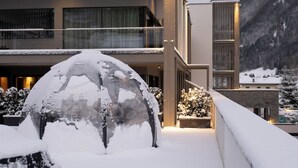 A modern building with a snow-covered entrance and a mountain backdrop. - Dolomiti Exclusive your mountain suite (San Giovanni di Fassa)