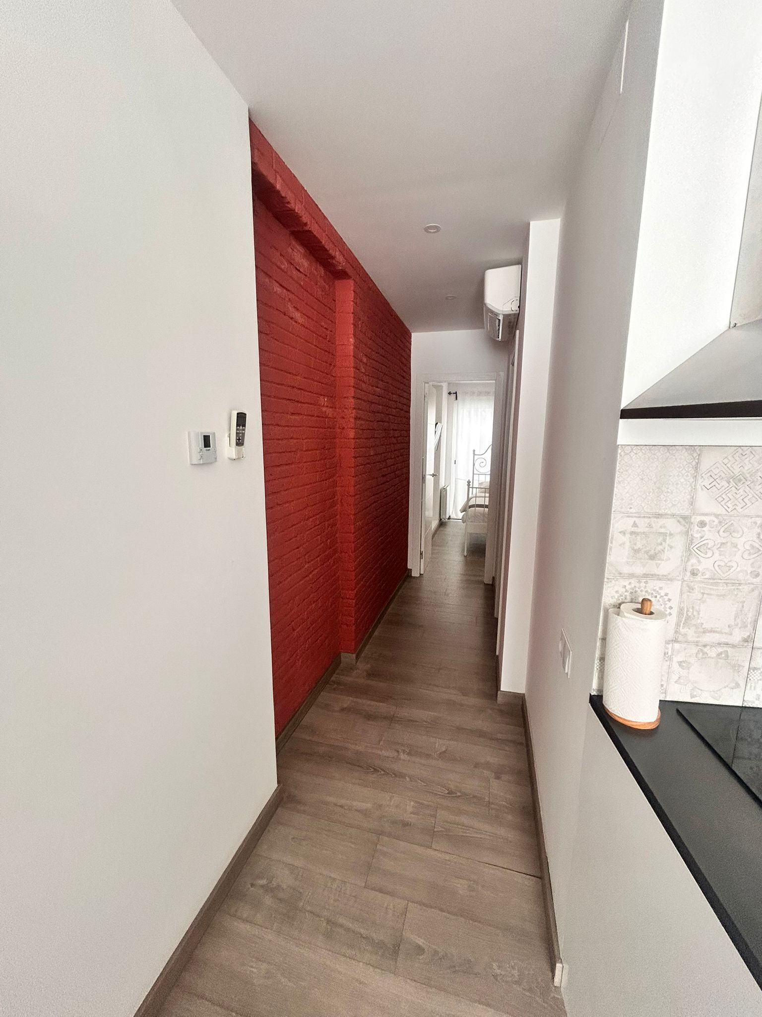 A modern hallway with a red brick accent wall, a wooden floor, and a black countertop with a paper towel holder.