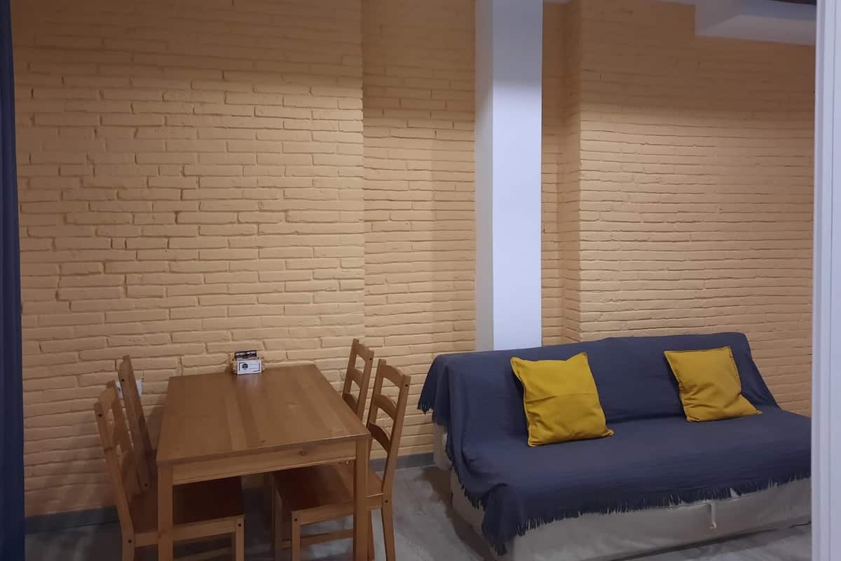 A room with a wooden table and chairs, a blue sofa with yellow cushions, and brick-patterned walls.