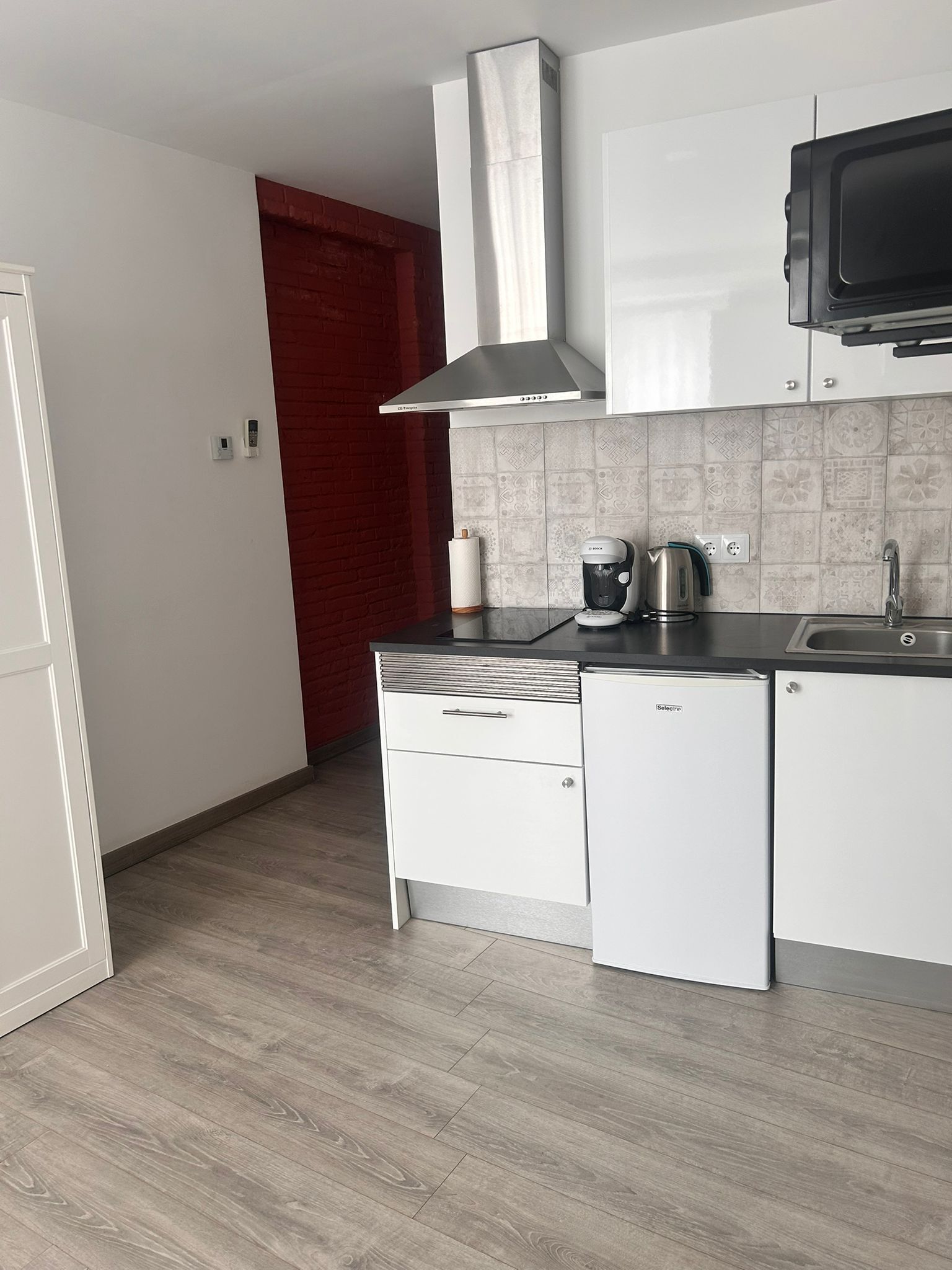 A modern kitchen with white cabinets, a stainless steel range hood, a coffee maker, and a microwave.