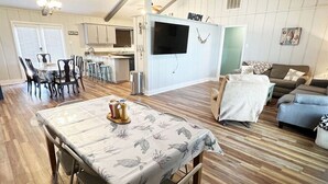 A spacious living area with a dining table, a sofa, and a TV mounted on the wall. - Reel Relaxn - Beach Access - Island Realty (Grand Isle)