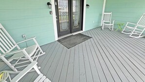 A porch with white rocking chairs and a door with a glass panel. - Reel Relaxn - Beach Access - Island Realty (Grand Isle)