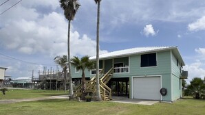 A light green building with a garage door, a staircase, and a small porch area. - Reel Relaxn - Beach Access - Island Realty (Grand Isle)