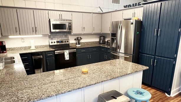 A modern kitchen with granite countertops, stainless steel appliances, and a dark blue cabinet. - Reel Relaxn - Beach Access - Island Realty (Grand Isle)