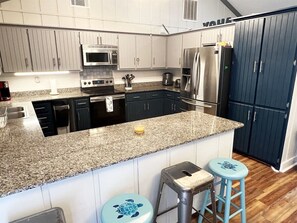 A modern kitchen with granite countertops, stainless steel appliances, and a dark blue cabinet. - Reel Relaxn - Beach Access - Island Realty (Grand Isle)