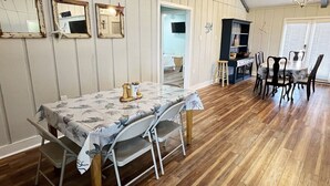 A dining area with a table set for four, surrounded by chairs, in a room with wooden flooring and white walls. - Reel Relaxn - Beach Access - Island Realty (Grand Isle)