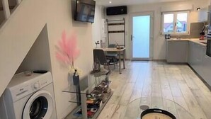 Un espacio habitable compacto con lavadora, comedor con sillas, televisor montado en la pared y zona de cocina con ventana.
