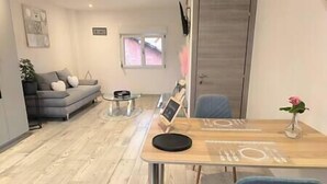 Una sala de estar moderna con un sofá gris, una mesa de centro de vidrio, una mesa de comedor con sillas y una pequeña planta en maceta.