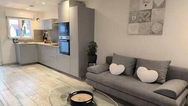 Una sala de estar moderna con un sofá gris, una mesa de centro de vidrio y una cocina al fondo.