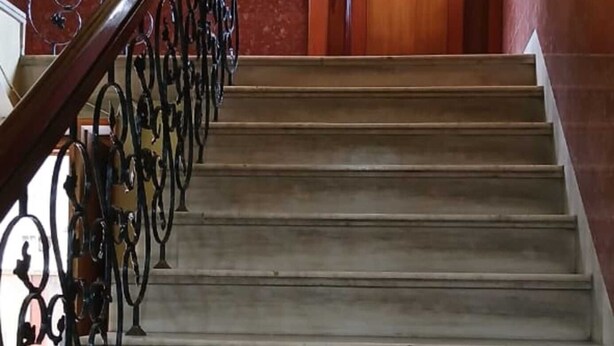 A staircase with a wooden handrail and metal balusters leading to an office door. - Hotel Sharda By Edge By GRB (Raipur)