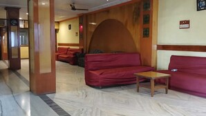 A hotel lobby with a marble floor, red sofas, a wooden coffee table, and a ceiling fan. - Hotel Sharda By Edge By GRB (Raipur)