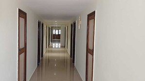 A long, narrow hallway with doors on both sides, leading to rooms. - Hotel Sharda By Edge By GRB (Raipur)