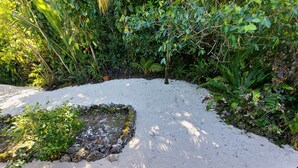 A bench in a garden with dense foliage and a sandy area. - Spatzy's Fale - Tropical Rainforest Retreat (Alofi)