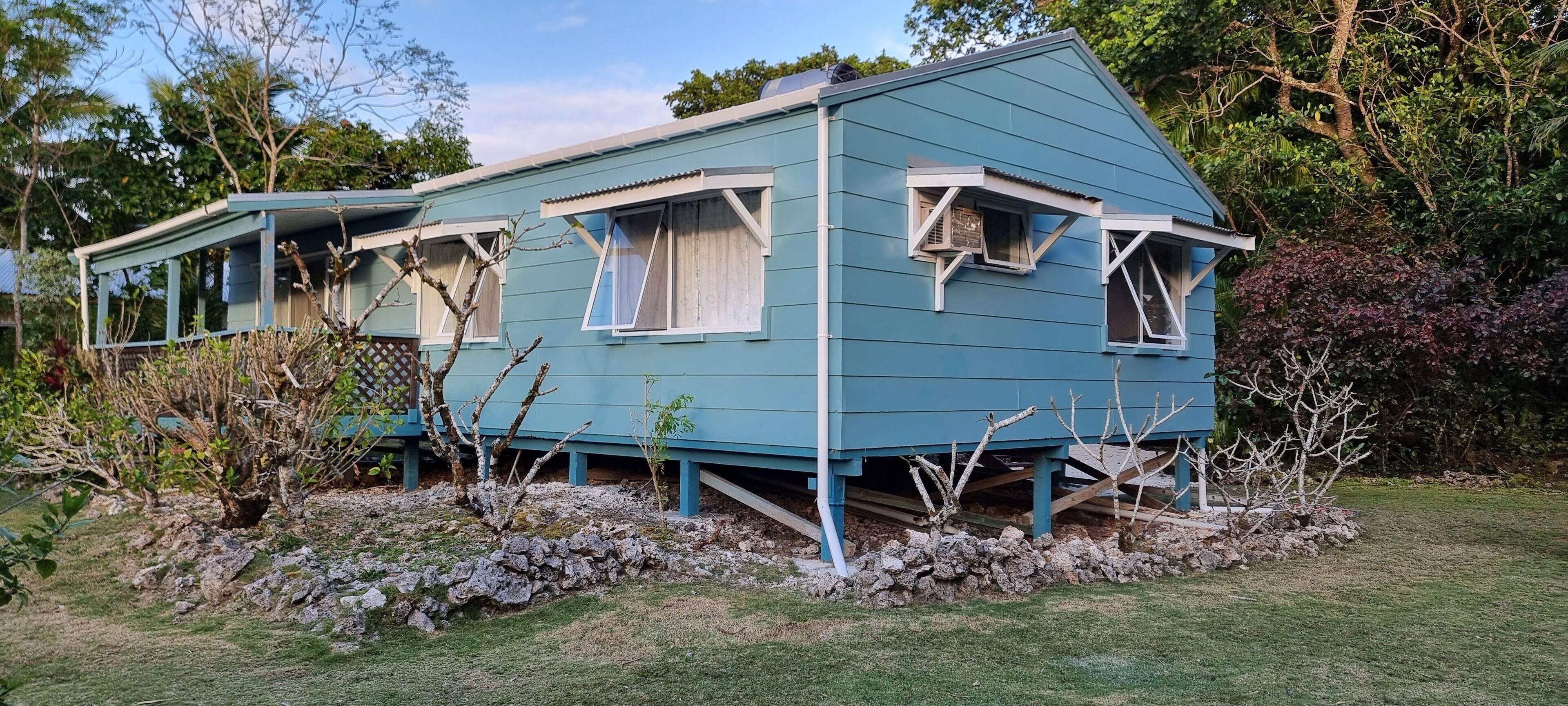 A blue house with multiple windows and a stone foundation.