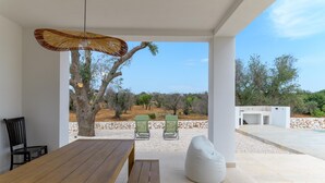 Une terrasse extérieure avec une table en bois, deux chaises vertes, un pouf blanc et un panier suspendu.
