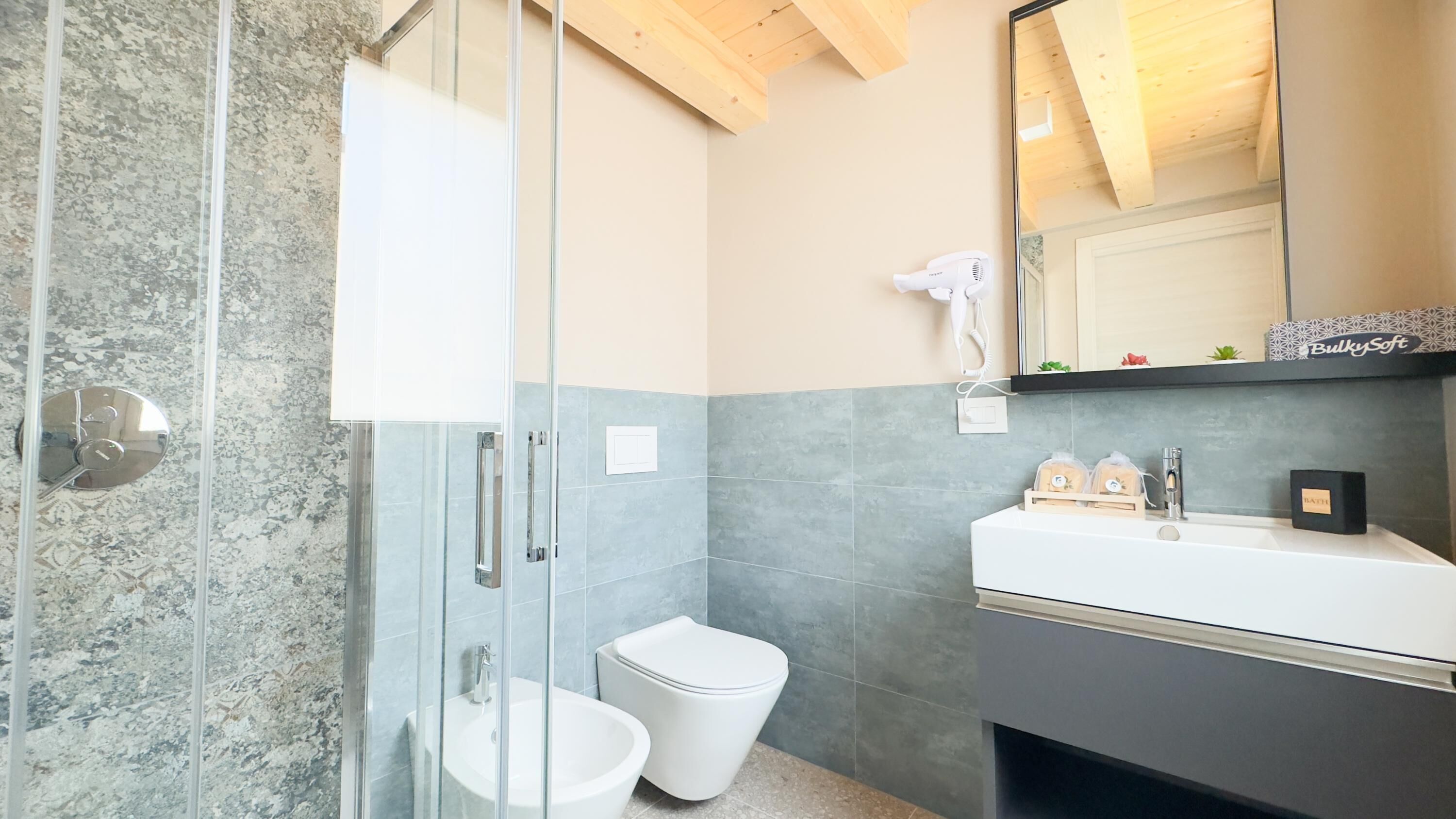 A modern bathroom with a glass shower enclosure, a white toilet, a sink with a mirror above, and a hairdryer on the wall.