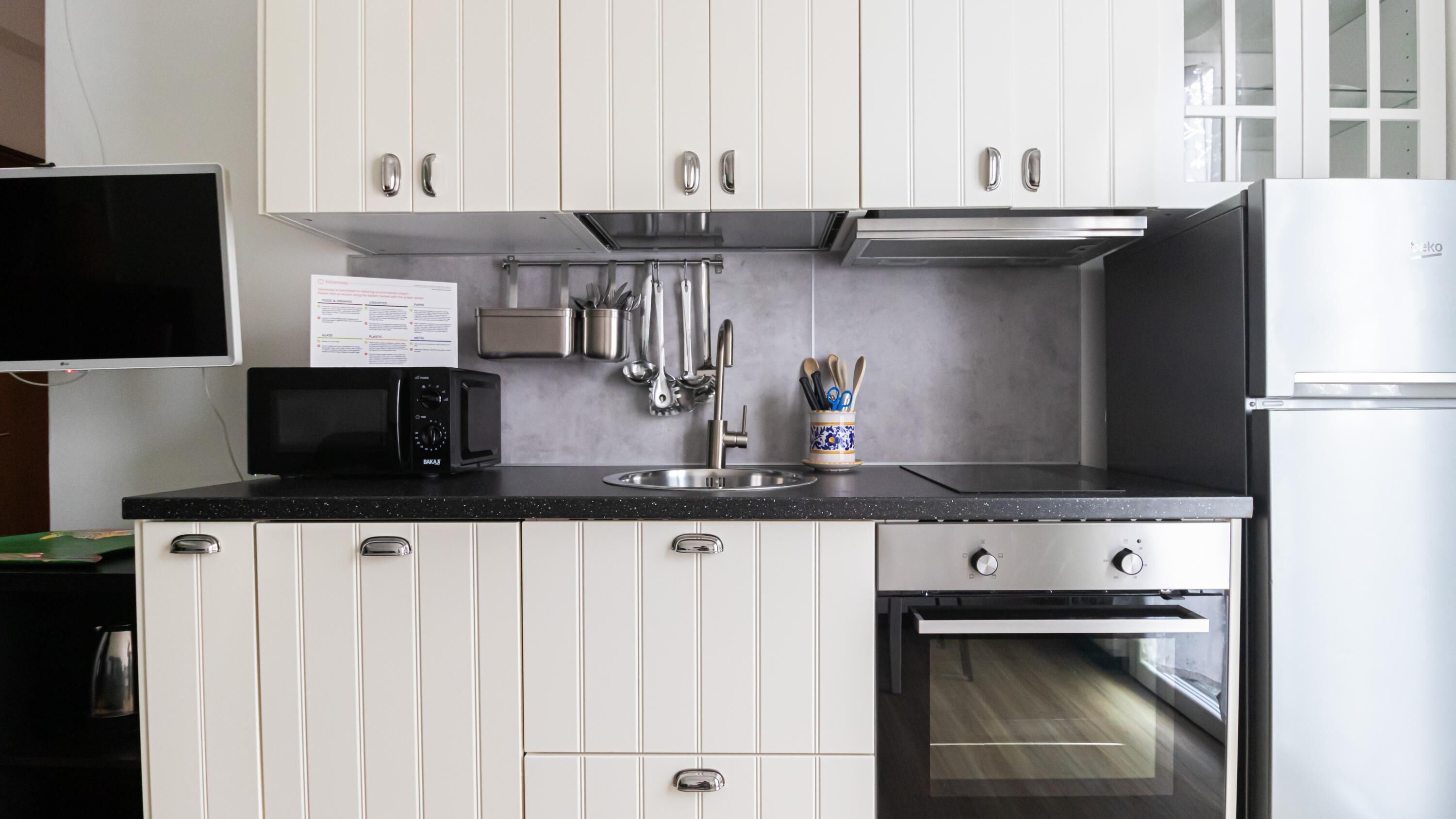 Une cuisine de taille réduite avec des meubles blancs, un plan de travail noir, un four à micro-ondes, un évier, une cuisinière et un réfrigérateur.