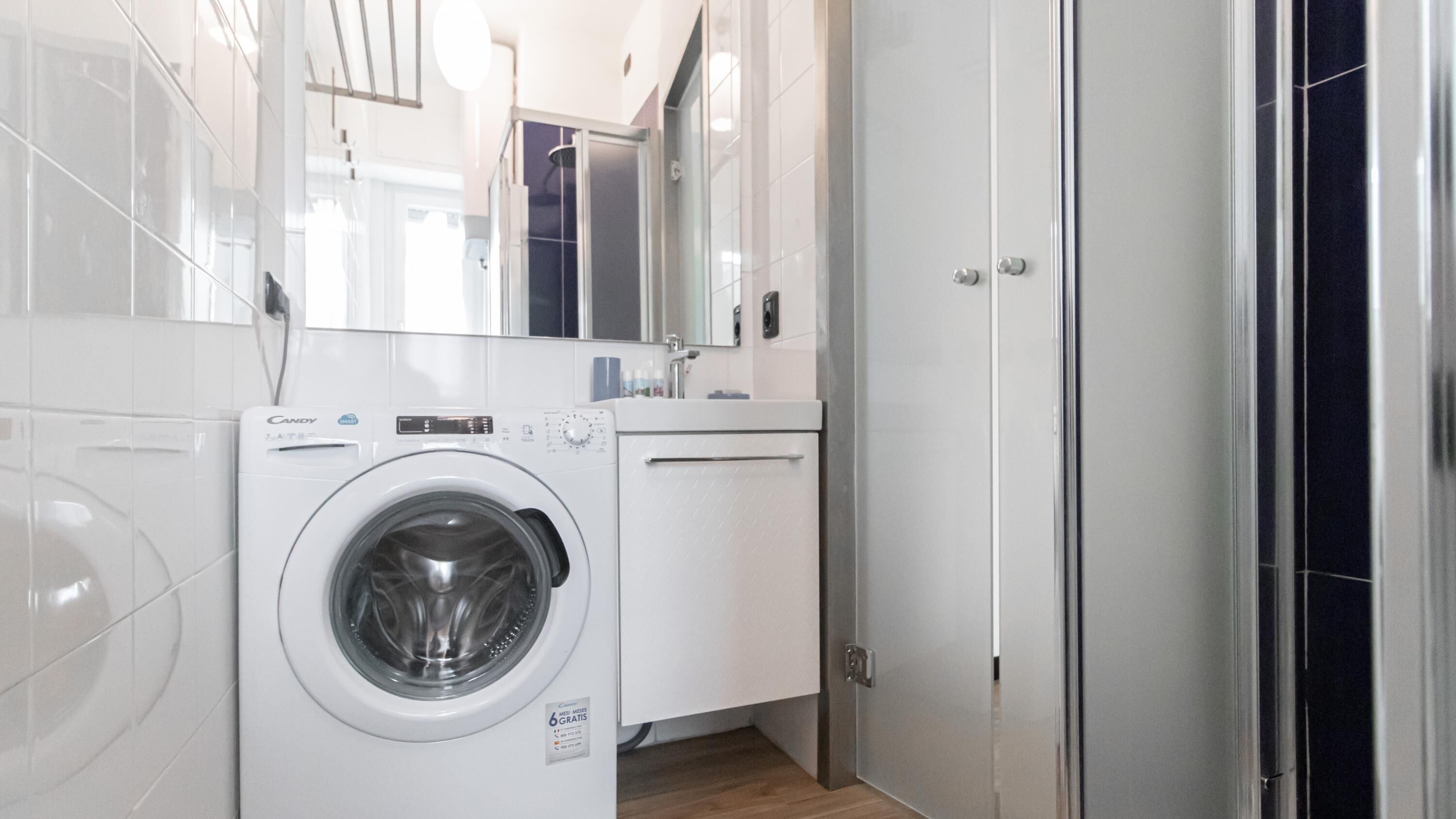 Een kleine, moderne badkamer met een ingebouwde wasmachine, een spiegel en een wastafel.