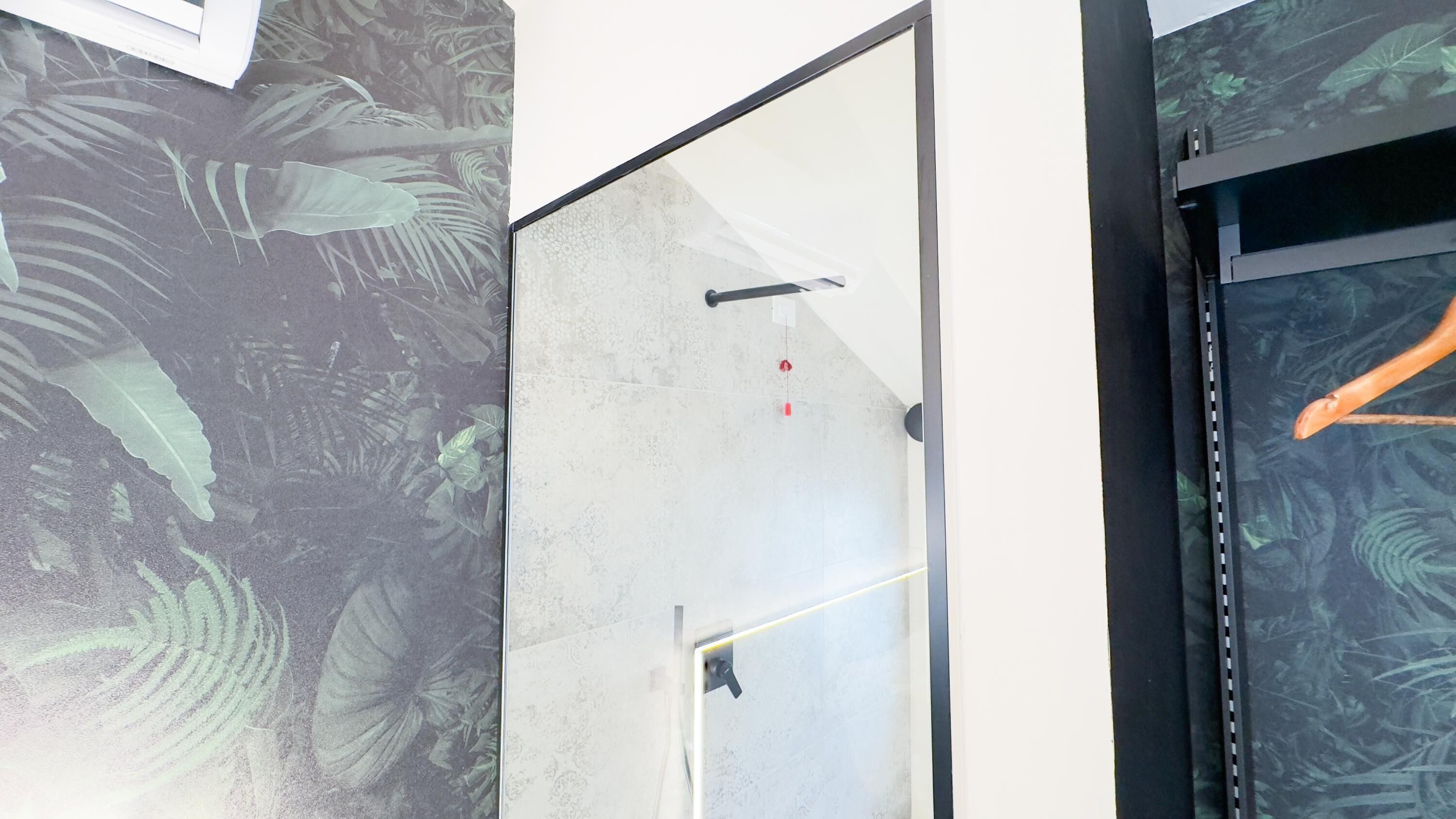 Un intérieur moderne avec un grand miroir, une porte blanche et un mur orné d’un motif de feuilles tropicales.
