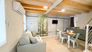 Una sala de estar moderna con un sofá gris, una mesa de comedor con sillas y una zona de cocina con un televisor montado en la pared.