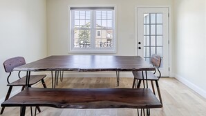 A dining area with a large wooden table and benches, a window with a view of a balcony, and a door with a glass panel. - Spacious 3BR Condo Near Ventnor Beach (Ventnor City)