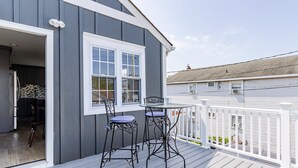 A deck with two metal chairs and a table, a white railing, and a gray building with a window and door. - Spacious 3BR Condo Near Ventnor Beach (Ventnor City)