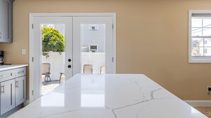 Una cocina con una isla grande de mármol, paredes color beige y vistas a un patio con sillas y una planta a través de una puerta.