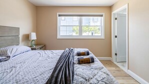 Un dormitorio con una cama, una mesita de noche, una lámpara, una ventana y una puerta.
