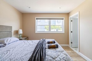 Ein Schlafzimmer mit Bett, Nachttisch, Lampe, Fenster und Tür.