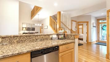 A kitchen with granite countertops, a dishwasher, wooden cabinets, a chandelier, and a staircase leading to another room.