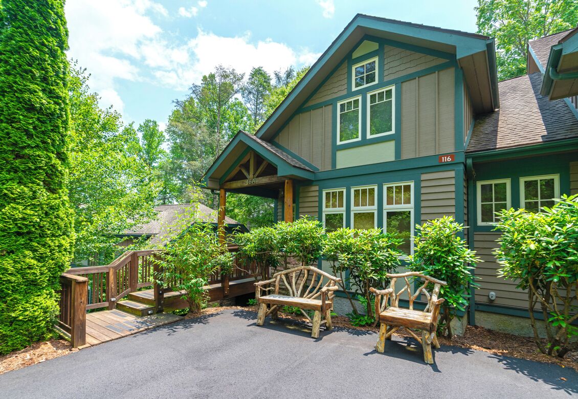 A two-story house with a porch, wooden benches, and a staircase leading to the entrance.