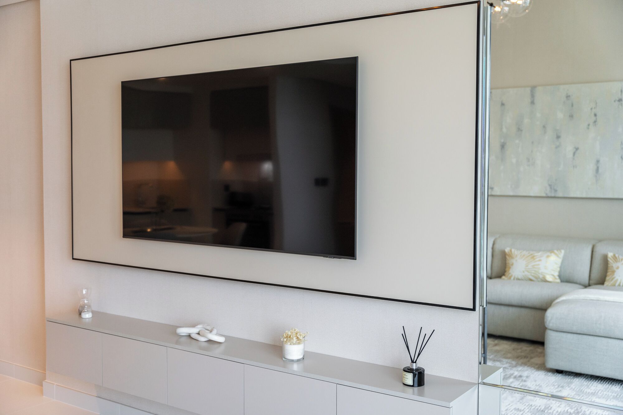 A modern living room with a large flat-screen TV mounted on the wall, a minimalist console table with decorative items, and a light-colored sofa in the background.