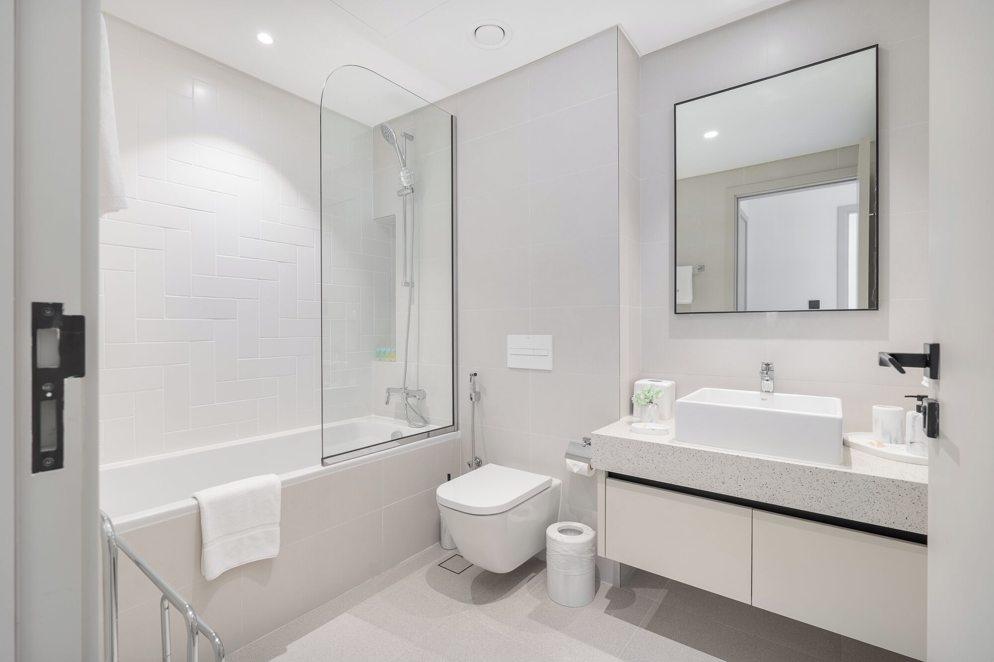 Une salle de bain moderne avec une douche à parois de verre, des toilettes blanches et un lavabo avec un miroir au-dessus.